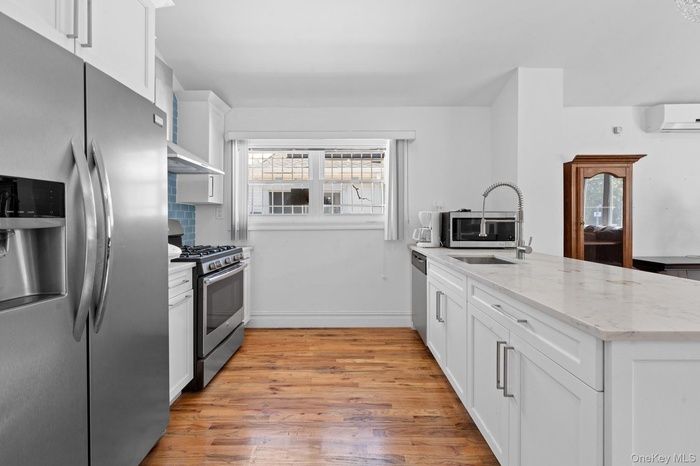 Kitchen featuring stainless steel appliances, white cabinetry, a peninsula, light stone countertops, and light wood-style floors