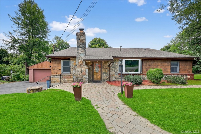 View of front of property featuring a front lawn, a garage, a shingled roof, a chimney, and stone siding