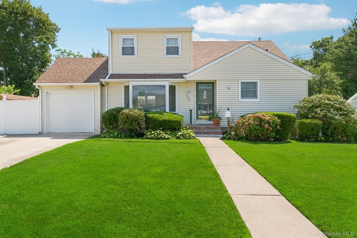 Traditional home featuring a garage, a shingled roof, and a front lawn