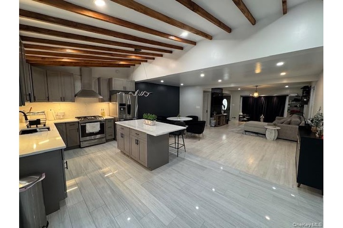 Kitchen with recessed lighting, stainless steel appliances, light stone counters, beamed ceiling, and a kitchen bar