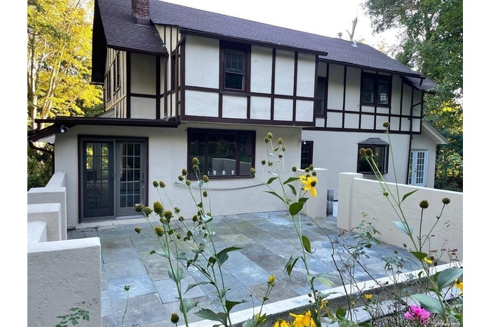 English style home with stucco siding, a shingled roof, a patio, and a chimney