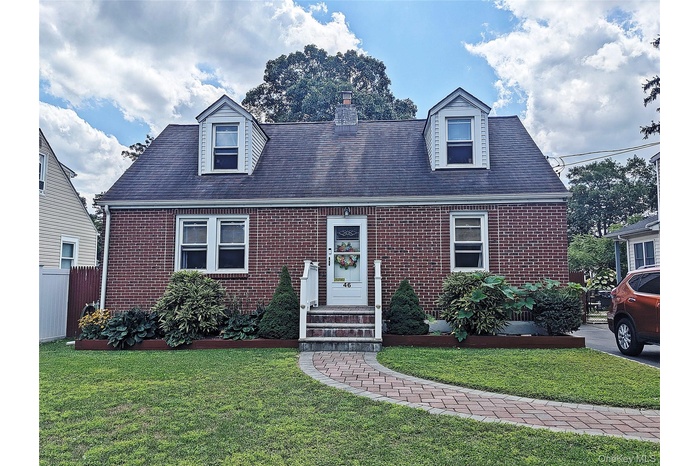 Cape cod-style house featuring brick siding, a chimney, and roof with shingles