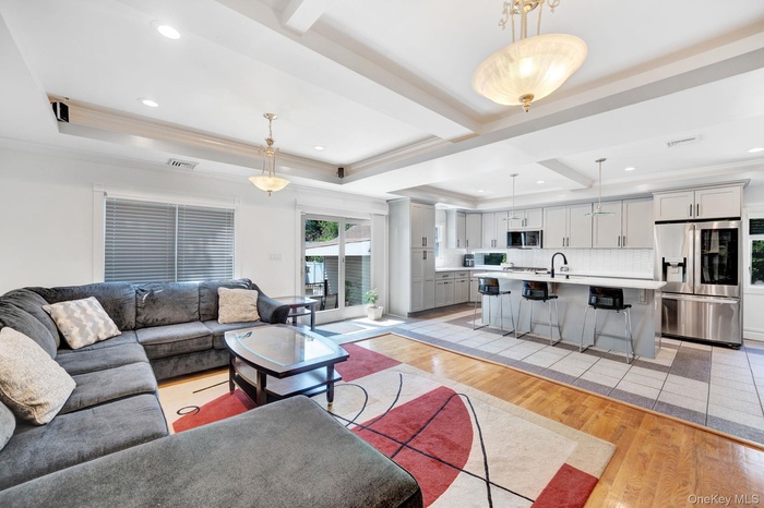 Living area with light wood finished floors, crown molding, a tray ceiling, recessed lighting, and beam ceiling