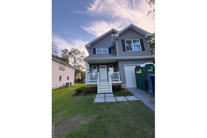 View of front of home with a front yard, covered porch, and a garage