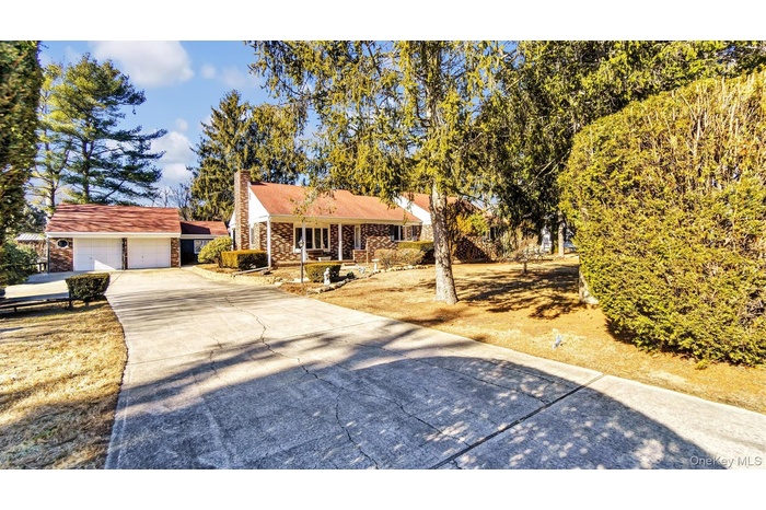 View of front facade with a garage, an outdoor structure, driveway, stone siding, and a chimney