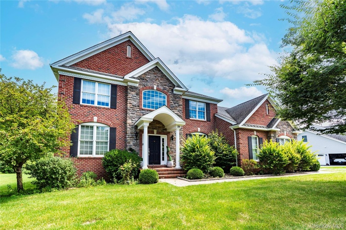View of front of property featuring brick siding, a front lawn, and stone siding