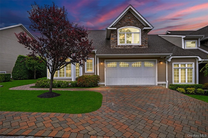 Traditional-style home featuring decorative driveway, a yard, a shingled roof, an attached garage, and stone siding
