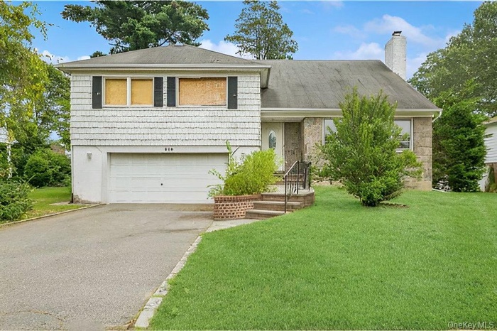 Split level home with an attached garage, asphalt driveway, a chimney, and a front yard