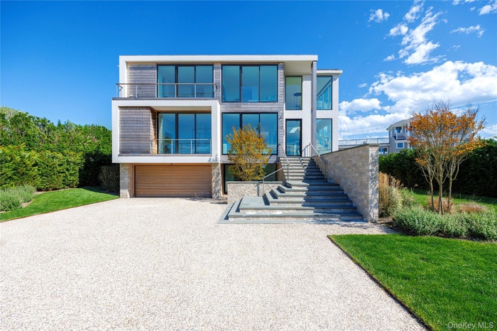 Modern home featuring driveway, an attached garage, stairs, and a front yard
