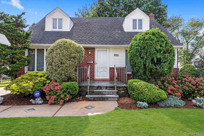 Cape cod-style house with brick siding, a shingled roof, a front lawn, and a chimney
