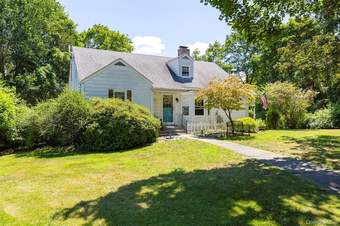 Cape cod-style house with a front lawn, roof with shingles, and a chimney