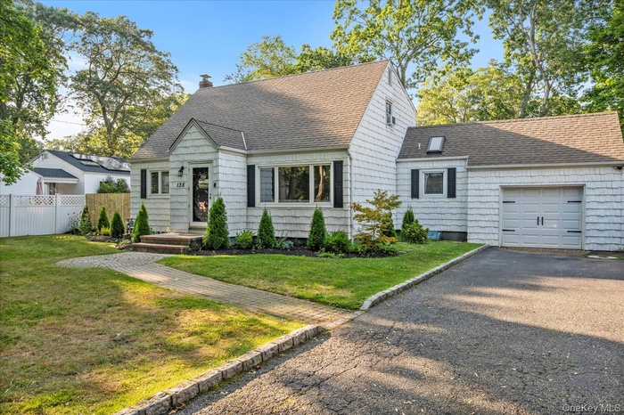 Cape cod home with a shingled roof, an attached garage, and driveway
