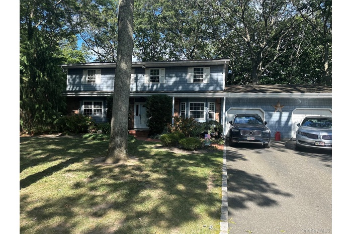 Traditional-style home with a garage, asphalt driveway, covered porch, and a front yard