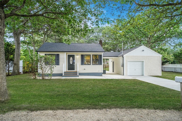 View of front of house with concrete driveway, a chimney, an attached garage, roof with shingles, and view of wooded area