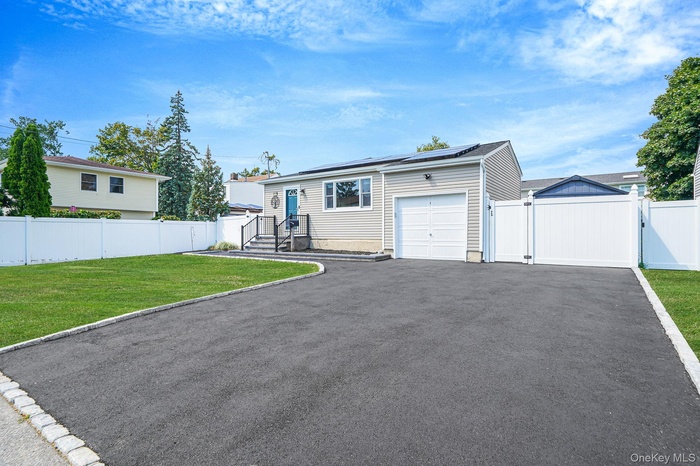 View of front facade featuring a gate, asphalt driveway, roof mounted solar panels, and a garage