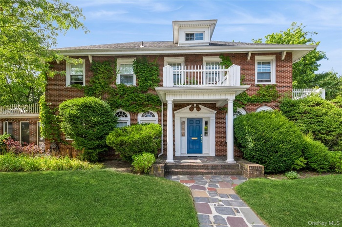 Colonial house with a balcony, a front lawn, and brick siding