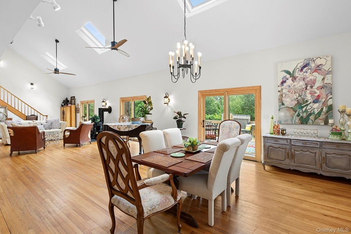 Dining room featuring a skylight, a ceiling fan, light wood-type flooring, a chandelier, and high vaulted ceiling
