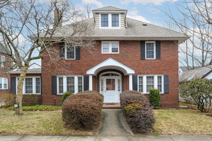 View of front facade featuring a shingled roof, a front yard, and brick siding