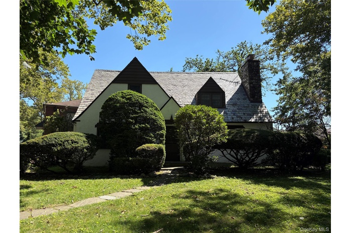 Tudor-style house featuring a high end roof, a chimney, a front yard, and stucco siding