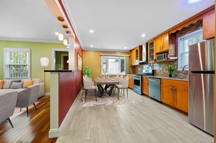 Kitchen featuring appliances with stainless steel finishes, decorative backsplash, brown cabinets, crown molding, and light wood-style flooring