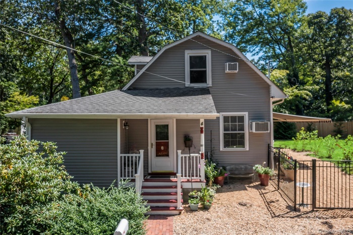 View of front of house with covered porch, roof with shingles, a gambrel roof, view of wooded area, and a gate