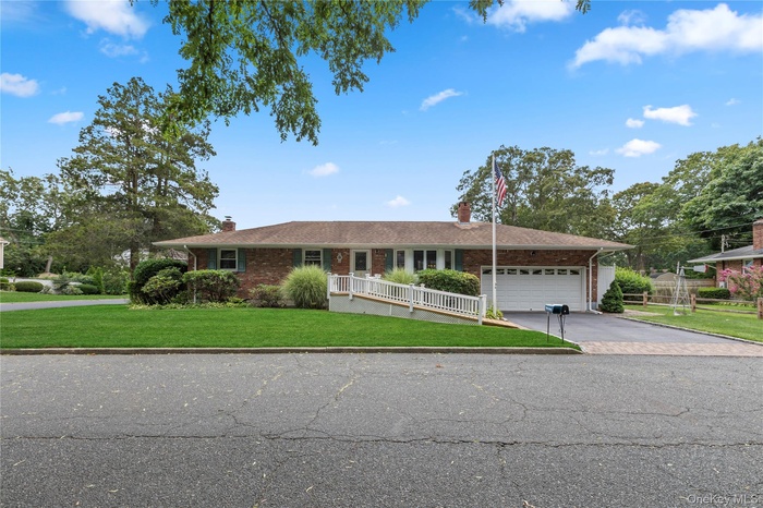 Ranch-style house featuring a chimney, driveway, brick siding, and an attached garage