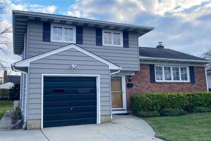 Home with an attached garage, driveway, a chimney, and brick siding