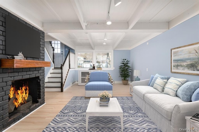 Living area featuring a fireplace, beam ceiling, light wood-style flooring, stairs, and a baseboard heating unit