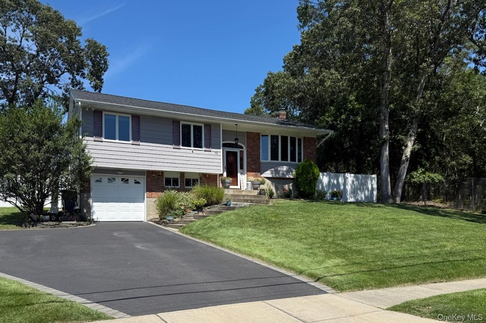 Split foyer home featuring brick siding, a garage, asphalt driveway, and a chimney