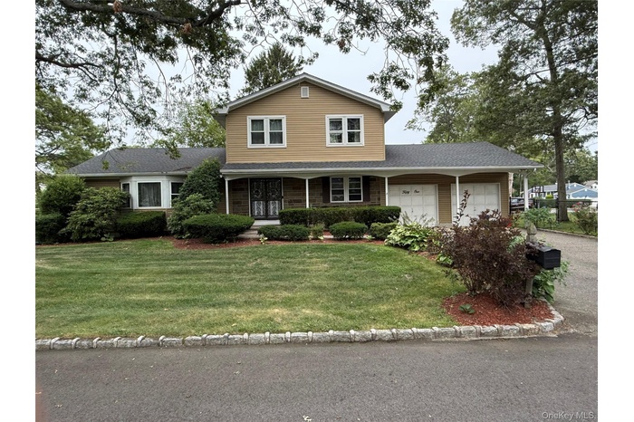 Traditional home featuring a porch, a front yard, a garage, roof with shingles, and driveway