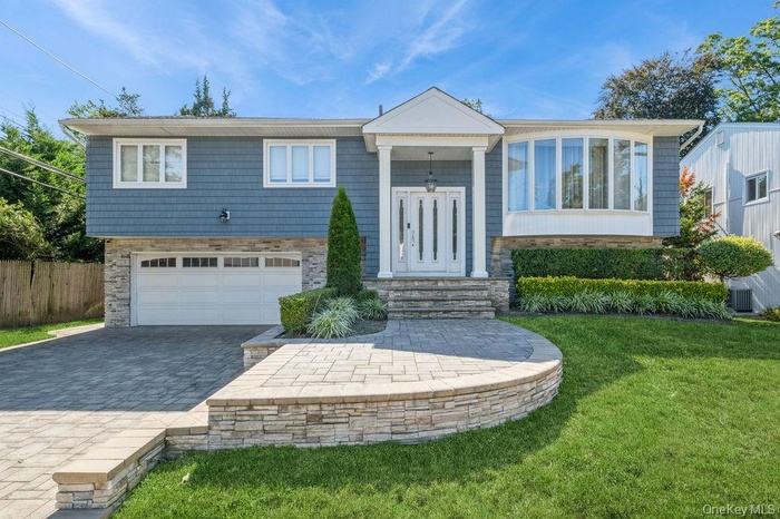 Split foyer home with decorative driveway, a garage, and stone siding