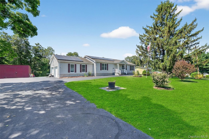 Ranch-style home with solar panels, driveway, an attached garage, and a front lawn
