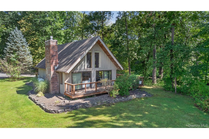 Rear view of house featuring a wooden deck, a chimney, a yard, a shingled roof, and board and batten siding