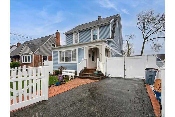 View of front of house with a gate, a patio, driveway, a chimney, and roof with shingles
