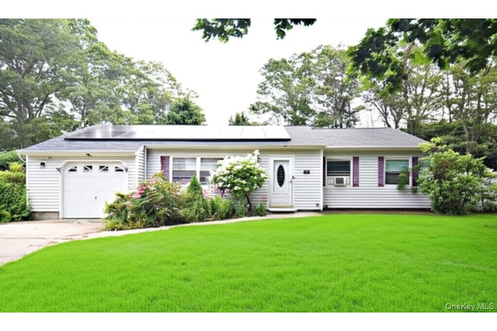 Ranch-style home with a garage, solar panels, a front lawn, and concrete driveway