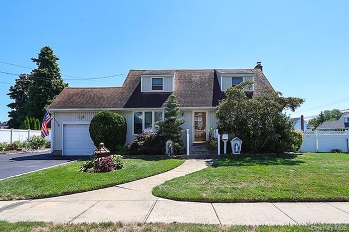 View of front facade with an attached garage, a chimney, asphalt driveway, and roof with shingles