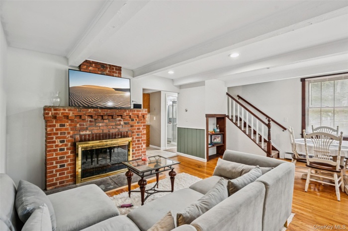 Living room with wood floors, stairway,  brick fireplace, beam ceiling, and wainscoted walls