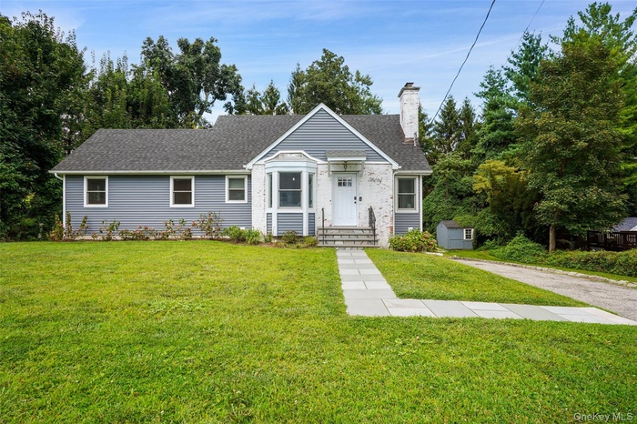 View of front facade with a front lawn, a shingled roof, and a chimney