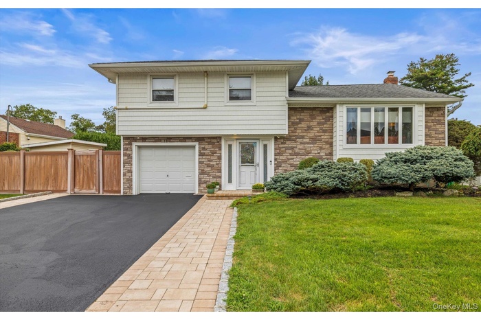 Split level home featuring stone siding, a garage, a chimney, asphalt driveway, and a shingled roof