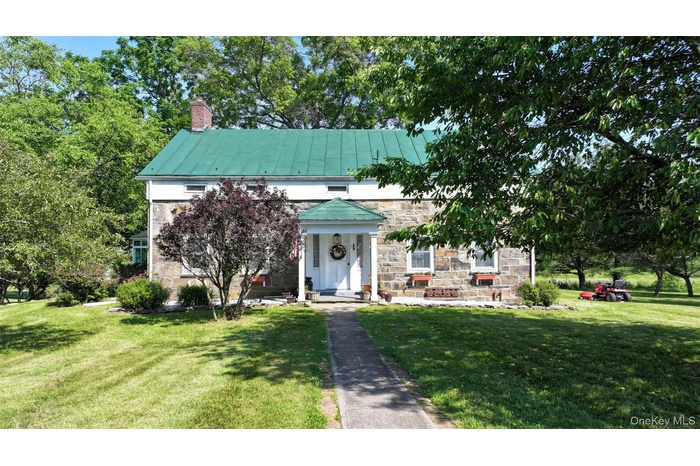 Colonial farm house featuring stone siding, a front lawn, a chimney, a standing seam roof, and a metal roof