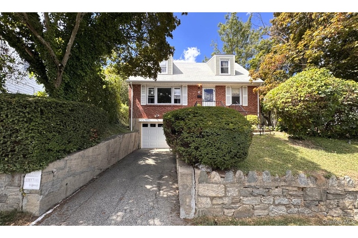 New england style home featuring a garage, brick siding, and driveway