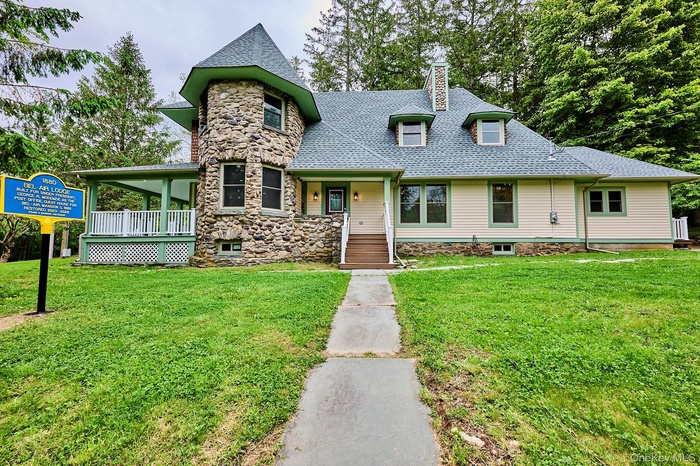 View of front of property with a chimney, a shingled roof, a front yard, and stone siding