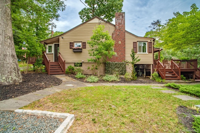 View of front facade featuring stairs, a front yard, a chimney, and a deck