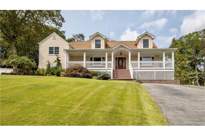 New england style home with a porch, a front yard, and roof with shingles
