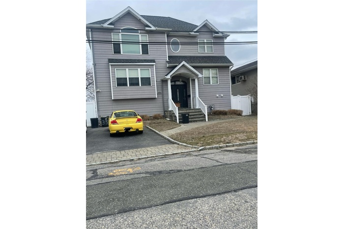 View of front facade with driveway, a shingled roof, and fence