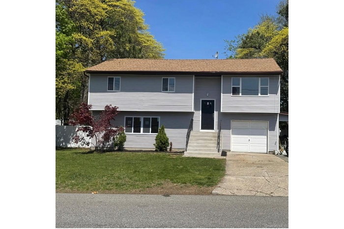 Raised ranch featuring entry steps, a garage, a front yard, driveway, and roof with shingles
