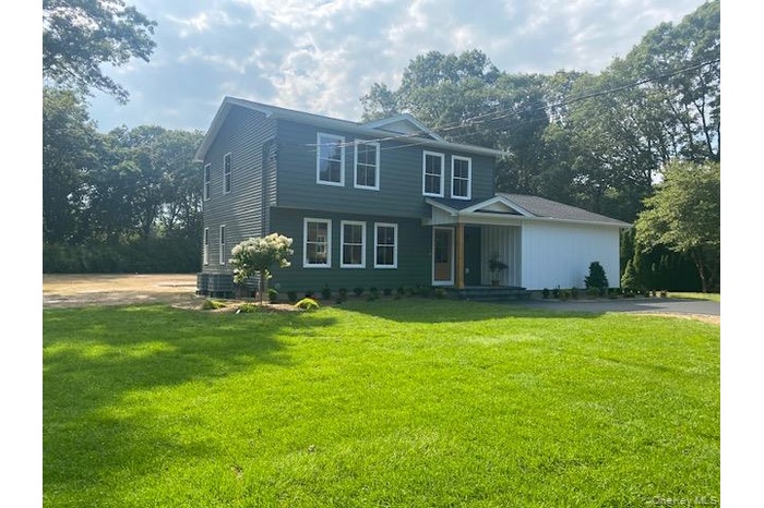View of front of property featuring a front yard, covered porch, and view of scattered trees