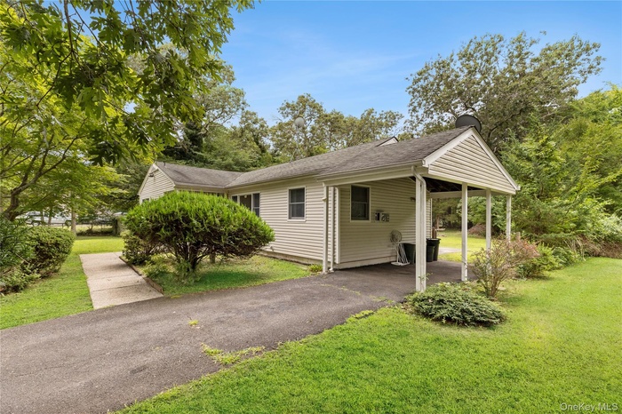 View of front of home featuring driveway, a front yard, an attached carport, and a shingled roof