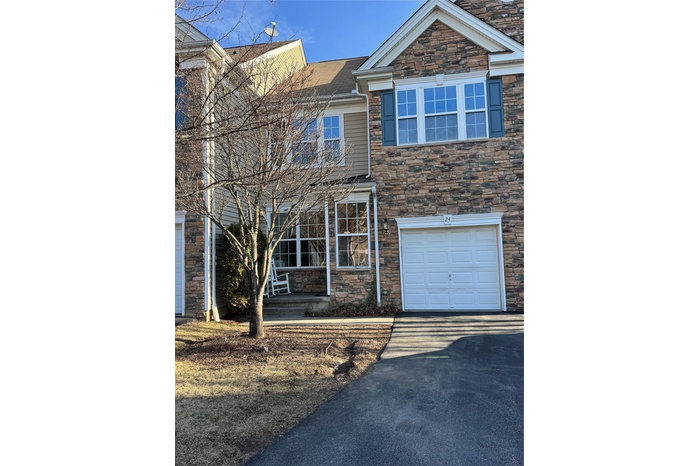 View of front of property with stone siding, an attached garage, covered porch, and driveway