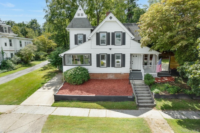 View of front facade with driveway, a shingled roof, and stairway